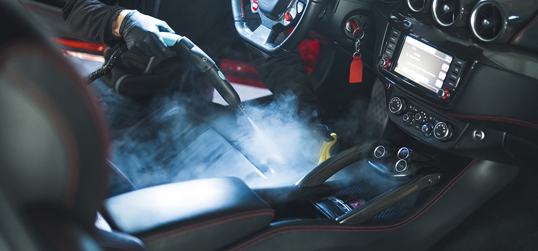 Lavage voiture haute pression : rinçage et mousse Lavage haute pression d'une voiture noire savonneuse sous un ciel bleu, l'eau mousse sur le capot et le pare-chocs.