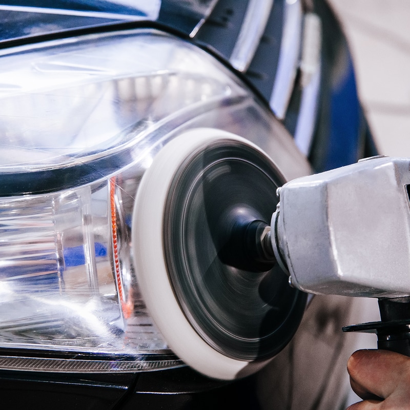 Restauration Phare Voiture : Polissage Anti-Jaunissement Polissage professionnel d'un phare de voiture jaunie avec une polisseuse rotative électrique à tampon en laine blanc.