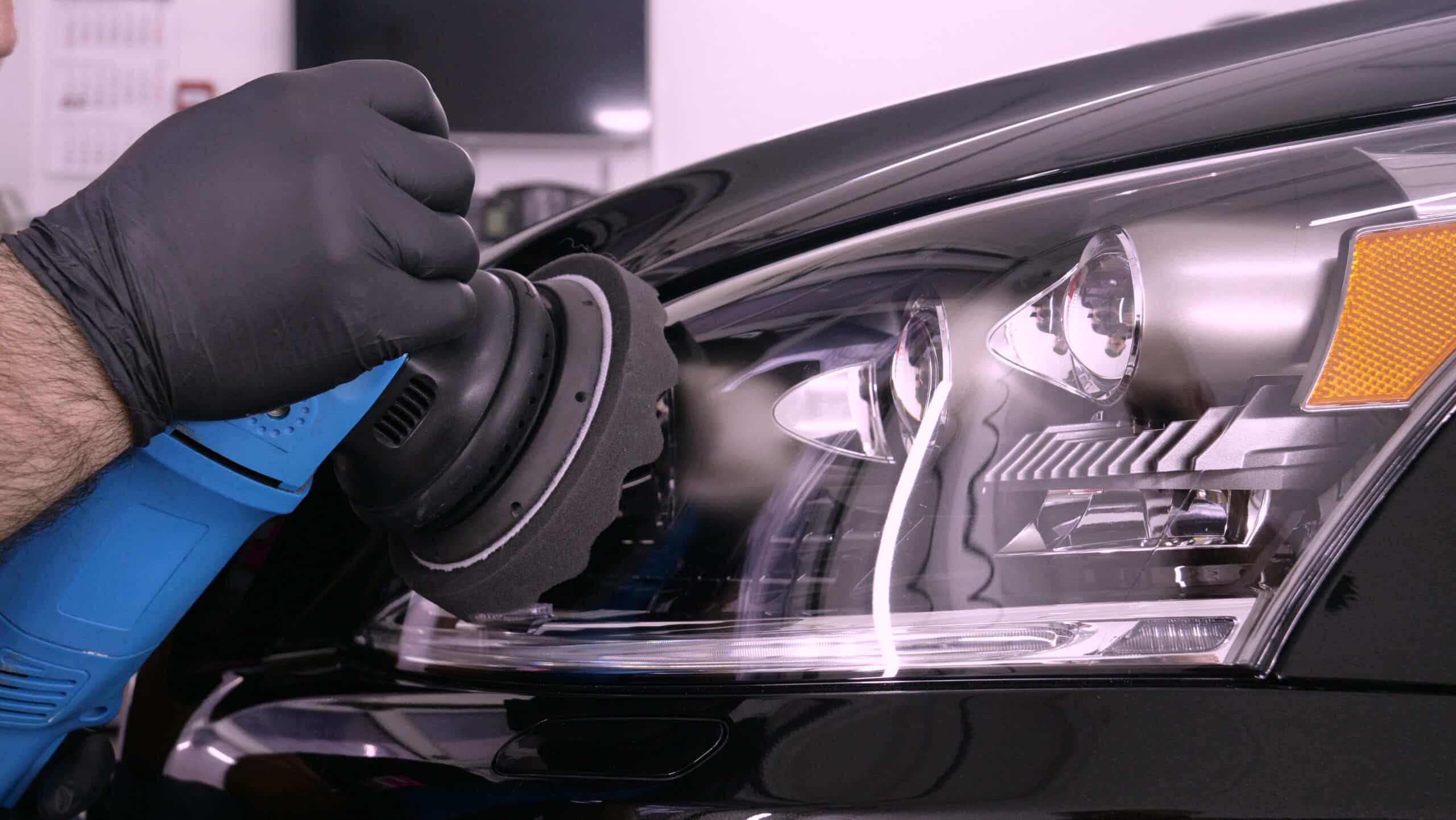 Lavage voiture haute pression : rinçage et mousse Lavage haute pression d'une voiture noire savonneuse sous un ciel bleu, l'eau mousse sur le capot et le pare-chocs.